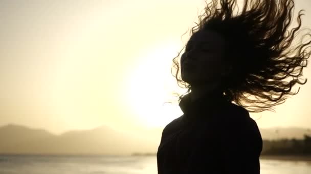 Slow Motion fermer silhouette de jeune femme déplaçant sa tête avec des cheveux soufflant dans le vent regardant le coucher du soleil sur l’océan. — Video