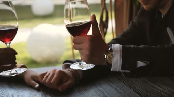 Primer plano de pareja amorosa cogida de la mano y tintineo vasos de vino tinto durante la cena romántica — Vídeo de stock