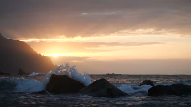 Τα κύματα αυξάνονται στον αέρα στο πανέμορφο ηλιοβασίλεμα στην παραλία Μπενίτζο στην Τενερίφη, τα Κανάρια νησιά. Το μεγάλο κύμα πέφτει σε βράχους και ψεκάζει. — Αρχείο Βίντεο