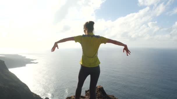 Giovane donna che alza le braccia su una bellissima scogliera ripida sull'oceano, vista dall'alto. Signora in vetta in uno splendido scenario . — Video Stock