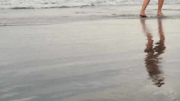 Tracking shot de atractiva joven trotando en la playa de arena negra en Tenerife, Islas Canarias. Mujer en fondo nublado junto al mar — Vídeos de Stock