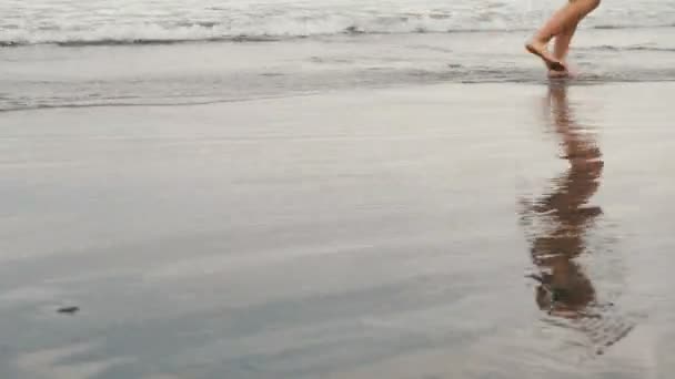 Tracking shot of attractive young woman jogging on black sand beach in Tenerife, Canary Islands. Female in cloudy seaside background — Stock Video