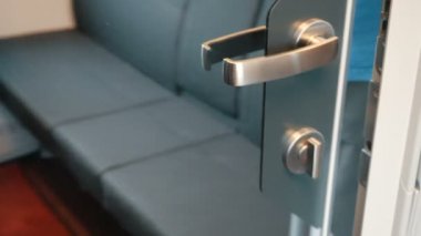 Siyah şortlu adam metal saplı bir ayna kapı açar ve modern rahat bir tren bölmesi girer. Bir tren yolcusu ayna kapısını içeriden kapatır ve mandallı kilitler..