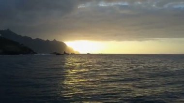 Ufukta güzel gün batımı ve dağlara bakan okyanus dalgaları üzerinde yavaş uçuş. Tenerife Benijo plajda güzel günbatımı ışık havadan drone atış, Kanarya Adaları, İspanya