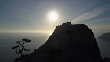 Mutlu genç kadın yüksek dağın tepesine tırmanıyor. Gün batımında kolları uzatılmış bir deniz üzerinde güzel bir manzara içinde zirveye ulaşan bayan.
