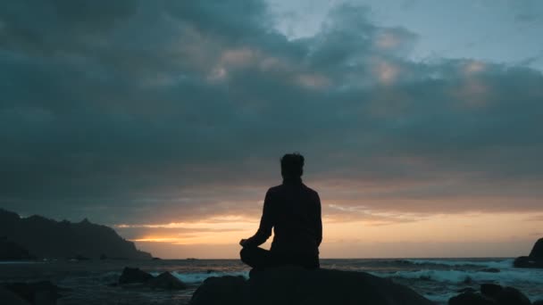 Tenerife, Kanarya Adaları Benijo plajda okyanus dalgaları gözlemleyerek gün batımında kayalar üzerinde oturan bir kadının silueti. — Stok video