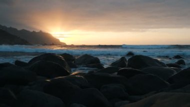 Yavaş çekim. Tenerife, Kanarya Adaları Benijo plajda güzel günbatımı ışık Okyanus Dalgaları. Büyük dalgalar kayalara çarpıyor ve püskürtüyor..