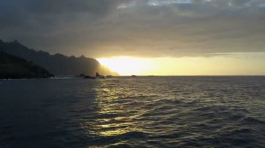 Ufukta güzel gün batımı ve dağlara bakan okyanus dalgaları üzerinde uçuş. Tenerife, Kanarya Adaları, İspanya'da güzel gün batımı havadan drone atış
