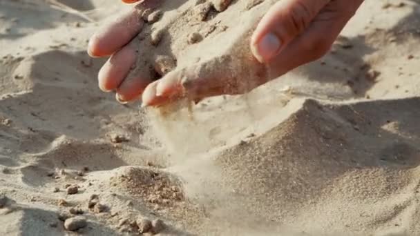 Slow motion, närbild: sanden passerar genom fingrarna på en ung kvinna. Sanden rinner genom fingrarna på en dam och sprids av en stark vind. — Stockvideo