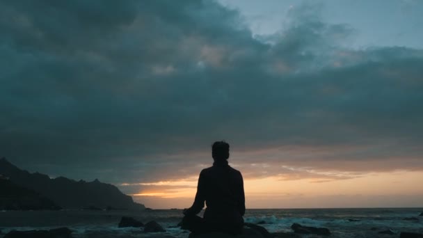 Силуэт женщины, сидящей на скалах на закате и наблюдающей океанские волны на пляже Бенихо на Тенерифе, Канарские острова . — стоковое видео
