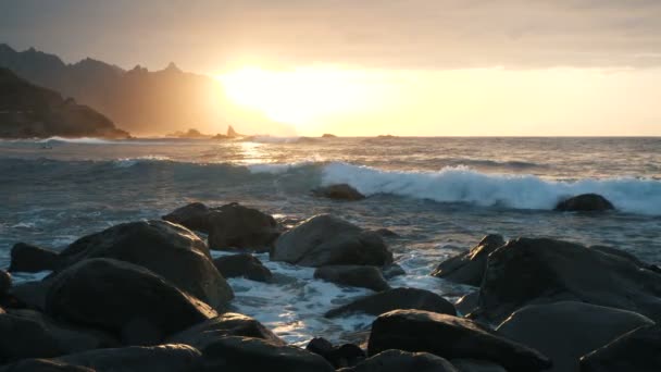 在加那利群岛特内里费岛的贝尼乔海滩, 海浪在岩石上拍打, 并在美丽的日落灯光下喷涌而下 — 图库视频影像