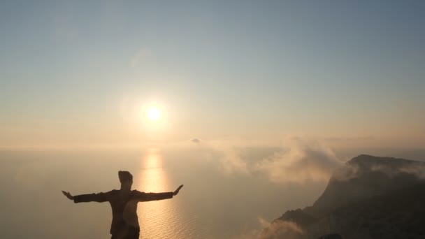 Silhuette Young Woman arms outstretched observing a beautiful dramatic sunset above a sea from a high mountain in Crimea. — Stock Video