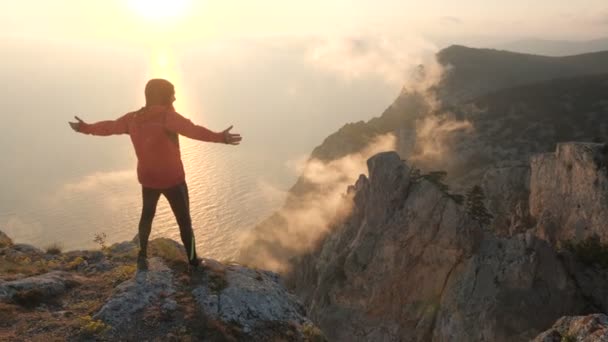 Silhuette van jonge man armen uitgerekt observeren prachtige dramatische kleurrijke zonsondergang boven een zee van een hoge berg in de Krim. — Stockvideo