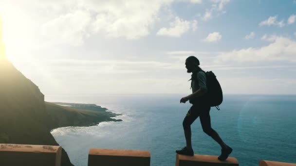 男性徒步旅行者带着背包在高高在海洋的金丝雀岛公路边缘行走的剪影. — 图库视频影像
