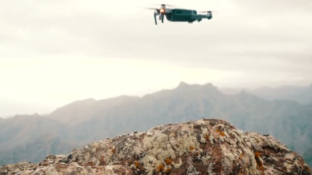 Primer plano de un dron de consumo aterrizando en una roca rugosa en lo alto de las montañas. Vista en cámara lenta, a nivel del suelo — Vídeos de Stock