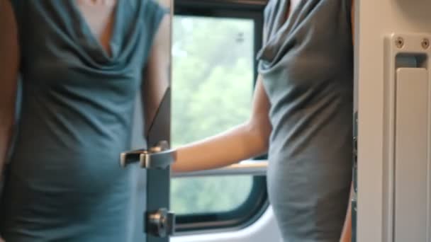 Una mujer joven abre una puerta de espejo con asa de metal y entra en un cómodo compartimento de tren moderno. Un pasajero del tren abre una puerta y toma asiento junto a la ventana . — Vídeos de Stock