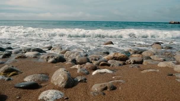 Les grosses vagues s'écrasent sur les pierres et pulvérisent au ralenti. Belle plage en Crimée avec des pierres et du sable. Caméra se déplace le long du littoral, vue latérale — Video
