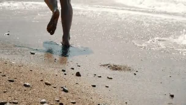 Activa mujer descalza deportiva corre a lo largo de la orilla del mar en cámara lenta. Movimiento lento: pies de las mujeres corriendo en la playa de arena caliente y soleada . — Vídeo de stock