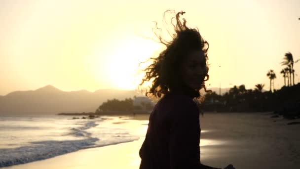 スローモーションクローズアップ海に沈む夕日を見ながら風に吹かれる髪のビーチでジョギングしている若い女性のシルエット. — ストック動画