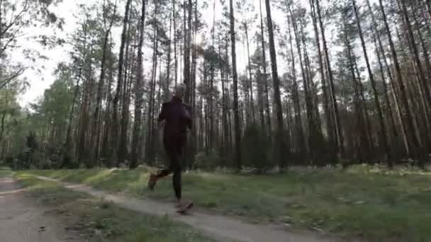 Happy young woman is jogging in a forest among trees. Tracking shot with stabilized camera — Stock Video