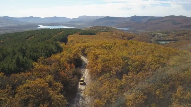 Vista aérea del coche que conduce a través del bosque en las montañas. Conducir por un hermoso camino de montaña en otoño. Tiro de trekking aéreo de un coche . — Vídeo de stock