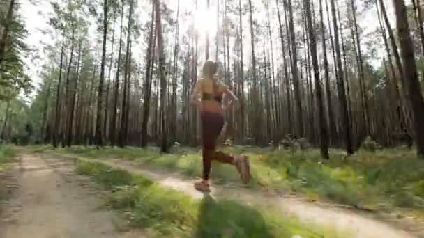 Happy young woman is jogging in a forest or in a park among trees. Tracking shot with stabilized camera — Stock Video