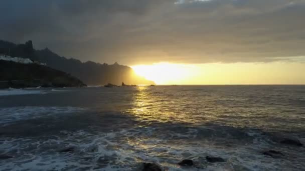 地平線上の美しい夕日と山に面した海の波の上の飛行。テネリフェ島、カナリア諸島、スペインの美しい夕日の空中ドローンショット — ストック動画