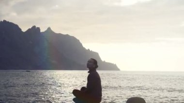 Tenerife, Kanarya Adaları'nda gün batımında kayaların üzerinde oturan ve okyanus dalgalarını gözlemleyerek bir kadının silueti.