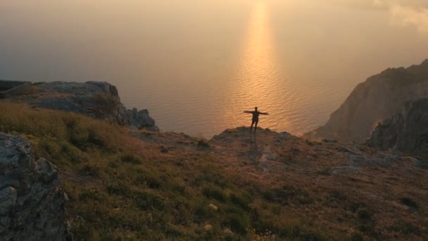 Silhuette de una mujer joven brazos extendidos observando una hermosa puesta de sol dramática sobre un mar desde una alta montaña en Crimea . — Vídeos de Stock