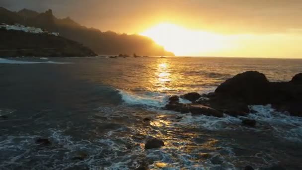Vista aérea. Las olas del océano chocan contra las rocas y rocían con la hermosa luz del atardecer cerca de la playa de Benijo en Tenerife, Islas Canarias . — Vídeos de Stock
