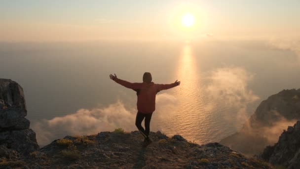 クリミアの高い山から海の上に美しい劇的なカラフルな夕日を観察する若者の腕のシルエットは伸びた. — ストック動画