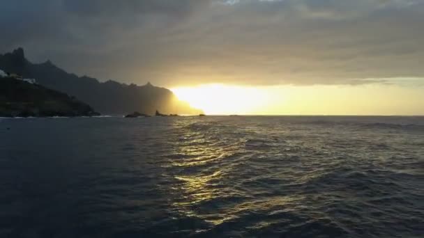 Lot wsteczny nad falami oceanu stoi piękny zachód słońca i góry na horyzoncie. Drone lotnicze strzał pięknego zachodu słońca na Teneryfie, Wyspy Kanaryjskie, Hiszpania — Wideo stockowe