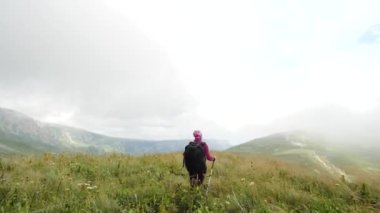 Sırt çantası olan genç kadın zirveye doğru yürüyor. Yavaş çekim. Bayan güzel Kafkas dağlarında yürüyüş.