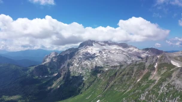 Tiro aéreo de um cume de montanha contra falésias rochosas, geleira e picos nevados. Vista aérea surpreendente de uma paisagem de montanha . — Vídeo de Stock