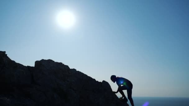Młody długowłosy inspirowany człowiek podnosi ręce się stojący na szczycie góry nad morzem przed pięknym błękitnym niebie. Sylwetka szczęśliwego hikera człowieka stojącego na szczycie. — Wideo stockowe