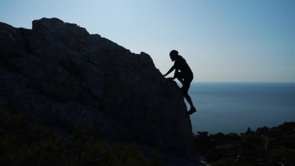 Joven hombre de pelo largo inspirado levanta sus manos de pie en la cima de una montaña sobre el mar contra el hermoso cielo azul. Silueta de un hombre caminante feliz de pie en la cumbre . — Vídeos de Stock