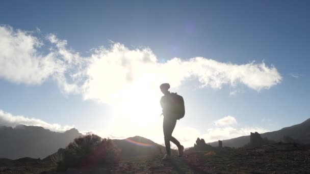 Silhouette d'une jeune randonneuse avec sac à dos montant vers le sommet contre le ciel bleu et les nuages au coucher du soleil. Au ralenti. Dame est randonnée dans de belles montagnes sur les îles Canaries . — Video