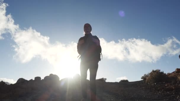 Silhouet van een jonge vrouw wandelaar met rugzak wandelen naar de top tegen blauwe hemel en wolken. Slow Motion. Lady is wandelen in prachtige bergen op Canarische eilanden. — Stockvideo