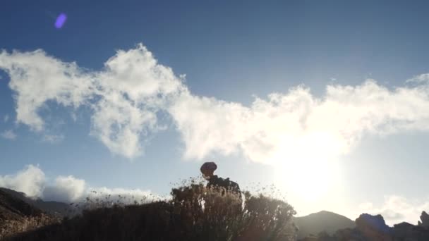 Sziluettje egy fiatal nő túró a hátizsákot gyaloglás felé csúcstalálkozó kék ég és a felhők. Lassított. Lady túrázás, gyönyörű hegyek a Kanári-szigeteken. — Stock videók