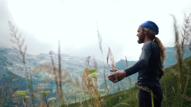 긴 머리를 가진 남자 등산객은 아름다운 전망과 주변야생 자연을 즐기는 산에서 손을 들어 올린다. 승리와 성공, 목표의 달성. — 비디오