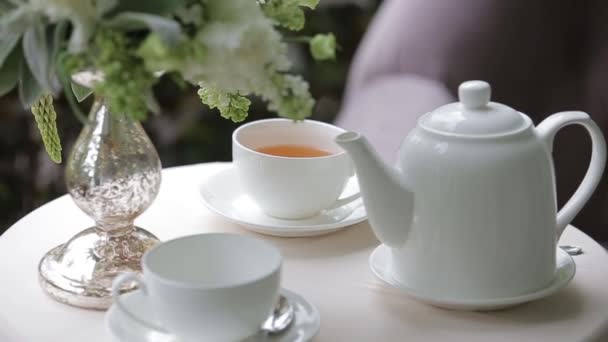 Gorąca herbata w białych filiżanek serwowane na białym stole ozdobiony bukiet kwiatów. Panorama ostrości. — Wideo stockowe