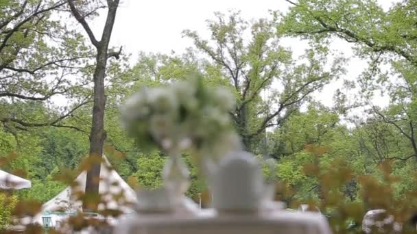 Té caliente en tazas blancas y tetera blanca servida al aire libre sobre una mesa blanca decorada con un ramo de flores. Panorama focal . — Vídeo de stock