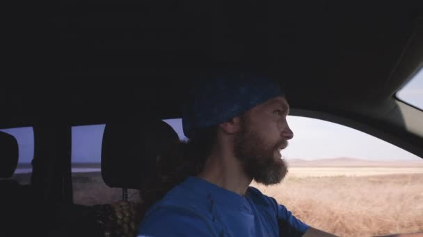 Feliz hombre barbudo conduce un coche en el paisaje rural. Olas del conductor mano inclinada por la ventana lateral — Vídeos de Stock