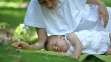 Anne açık havada yeşil bir çim engebeste uyuyan bebeğini öper. Green Summer Park'taki mutlu genç anne ve çocuk. Bahar parkında doğanın tadını çıkaran güzel aile.