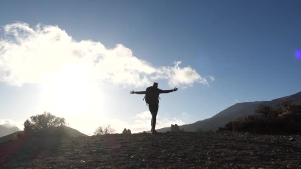 Σιλουέτα μιας νεαρής γυναίκας με σακίδιο που περπατάει ανηφόρα προς την κορυφή εναντίον του γαλάζιου ουρανού και των νεφών κατά το ηλιοβασίλεμα. Αργή κίνηση. Η κυρία είναι πεζοπορία σε πανέμορφα βουνά στα Κανάρια νησιά. — Αρχείο Βίντεο