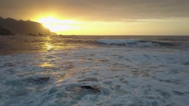 鸟瞰。在加那利群岛特内里费的贝尼霍海滩，低空飞行在海浪中升起。美丽的日落光在海洋表面. — 图库视频影像