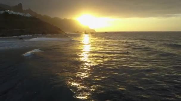 Вид с воздуха на океанские волны в красивом закате возле пляжа Бенихо на Тенерифе, Канарские острова. Серфингисты плавают по поверхности океана — стоковое видео