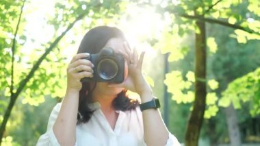 Güzel gülümseyen ve beyaz gömlek giyen gülen kız fotoğrafçı yeşil yeşillik yumuşak bir arka plan üzerinde bir parkta fotoğraf yapıyor ve su püskürtme.