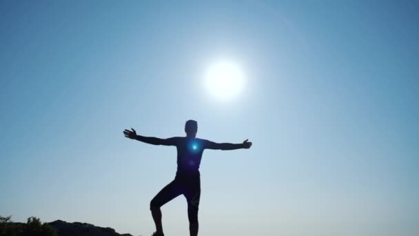 Młody długowłosy inspirowany człowiek podnosi ręce się stojący na szczycie góry nad morzem przed pięknym błękitnym niebie. Sylwetka szczęśliwego hikera człowieka stojącego na szczycie. — Wideo stockowe