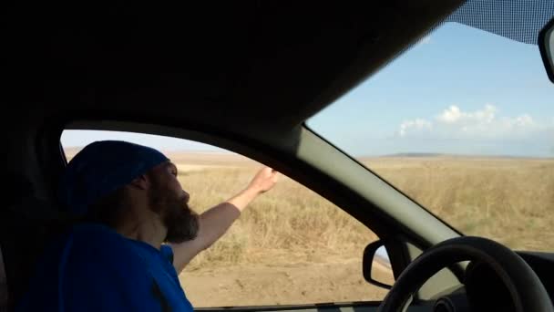 Щасливий бородатий чоловік водить машину в сільський пейзаж. Водійські хвилі рука виходить з бічного вікна — стокове відео